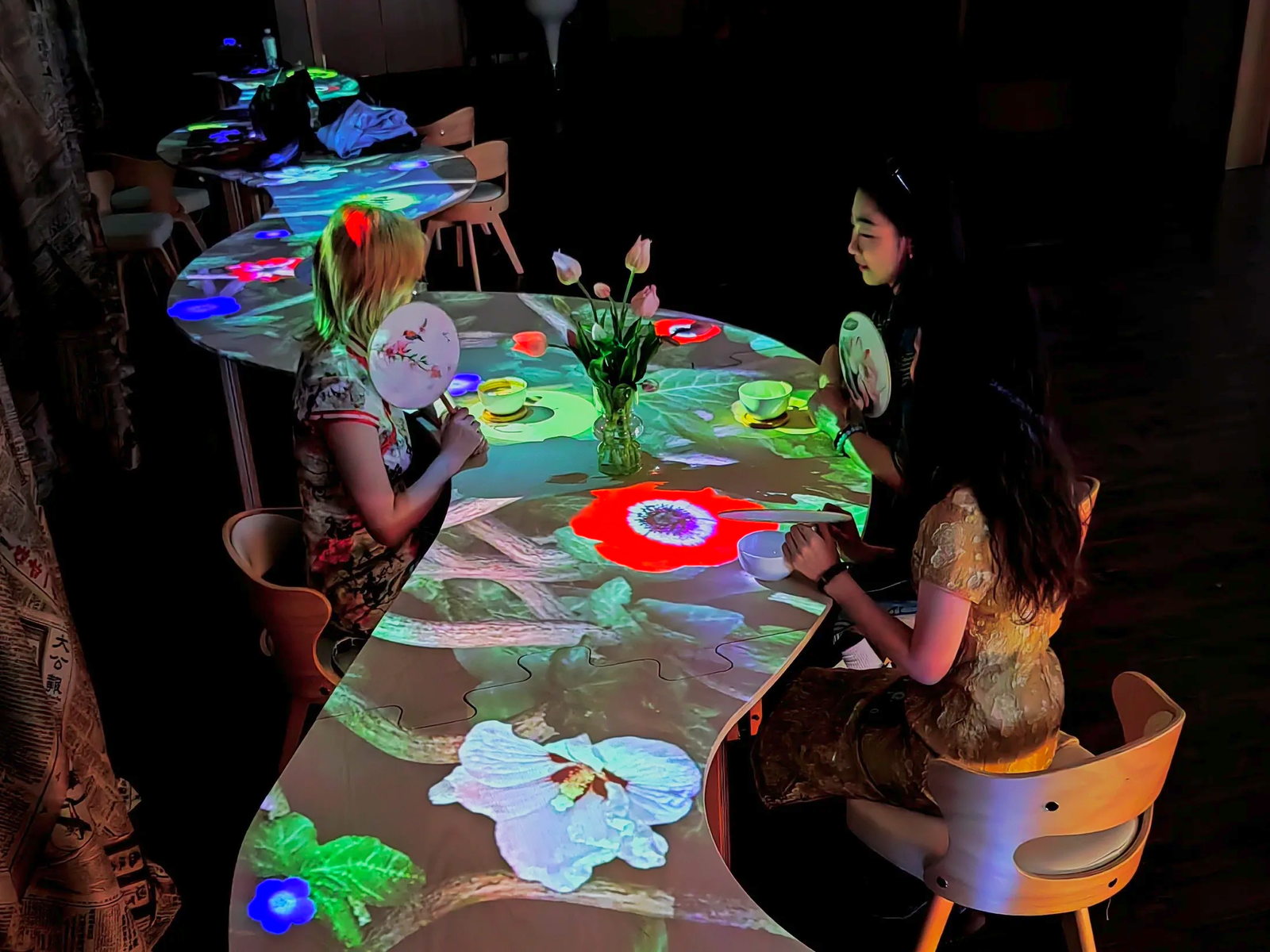 Visitors around the real café table with projected flowers, cups and a vase